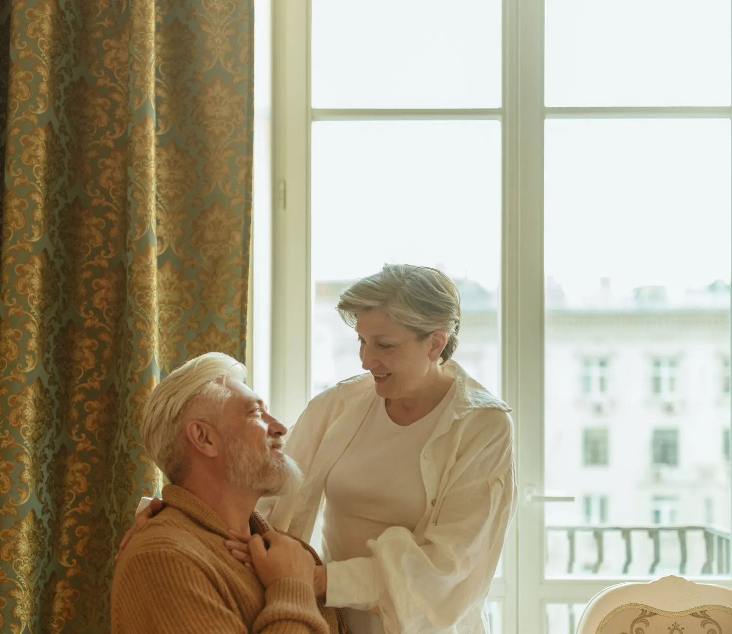 An older man and his adult daughter talking by a window at home