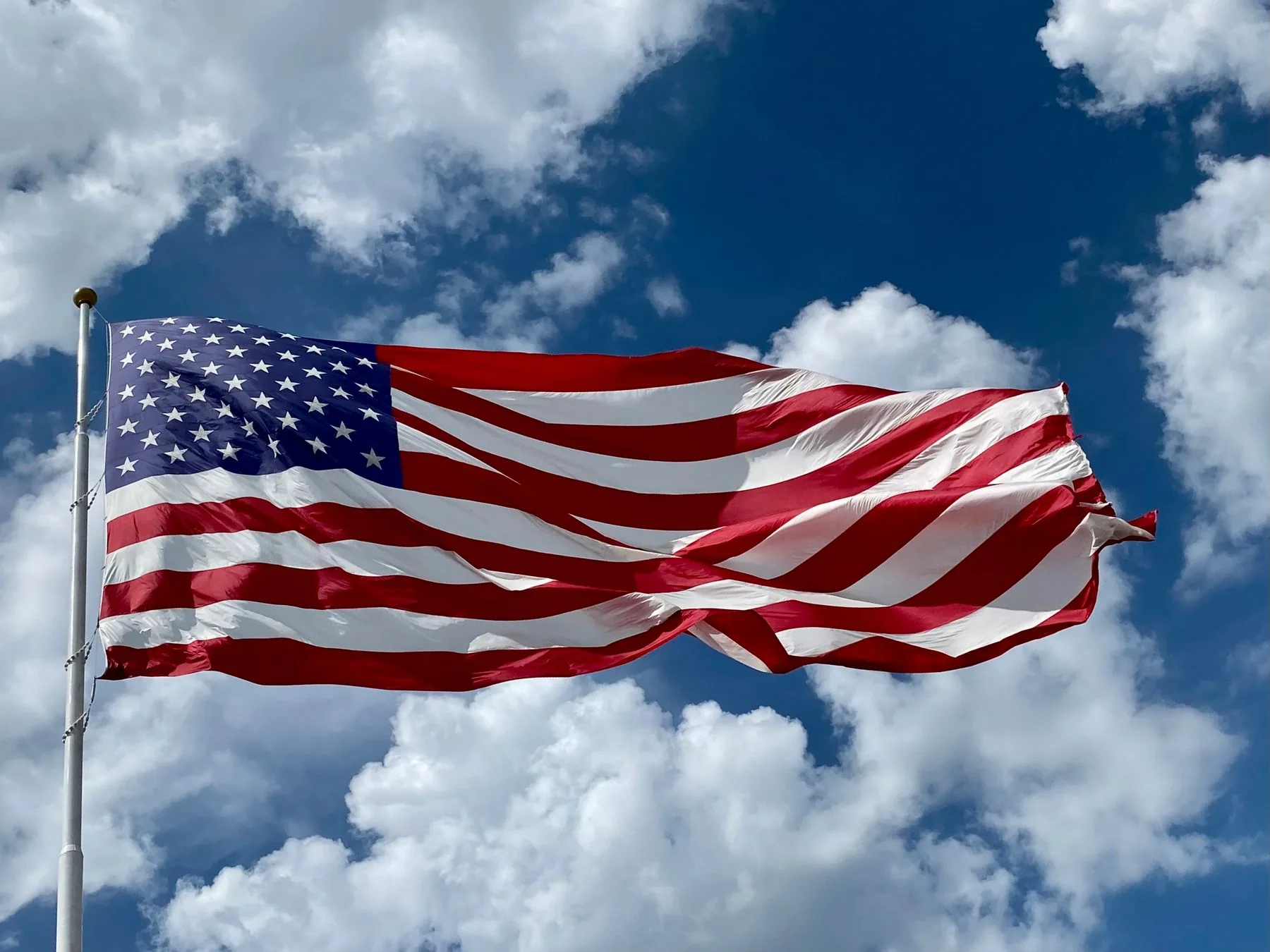 The American flag flying on a pole against a cloudy blue sky