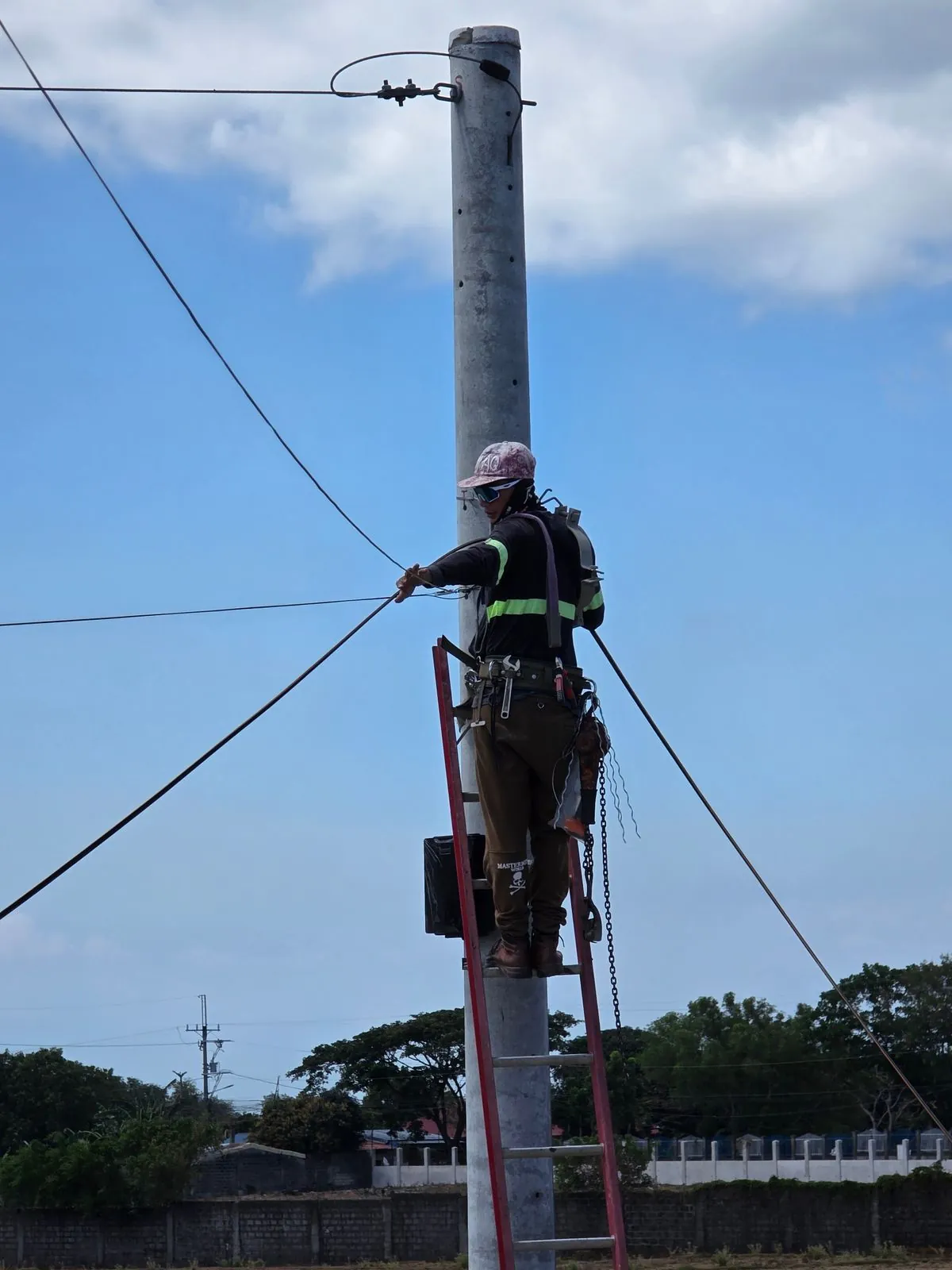 A lineman in a harness working at the top of a utility pole